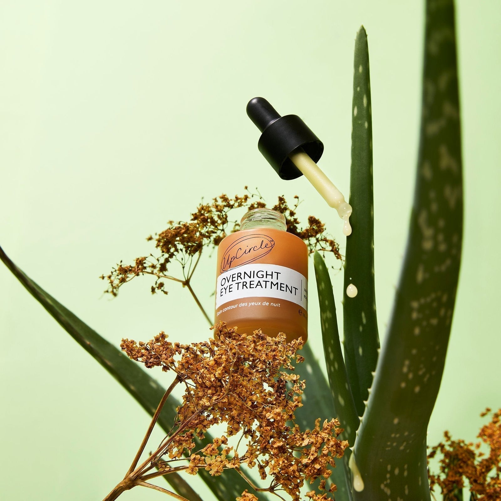 Open Eye Treatment bottle + pipette with sea weed and elderflower on a green background